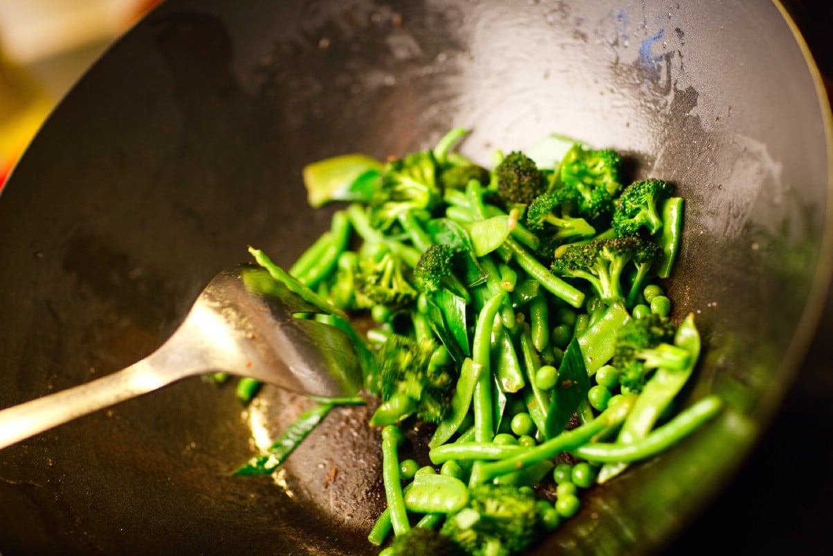Green vegetables being cooked in an electric wok.