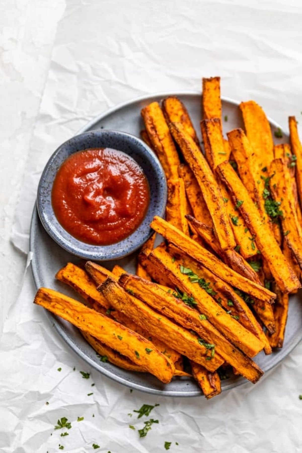 Sweet potato fries on gray plate with bowl of ketchup on marble table