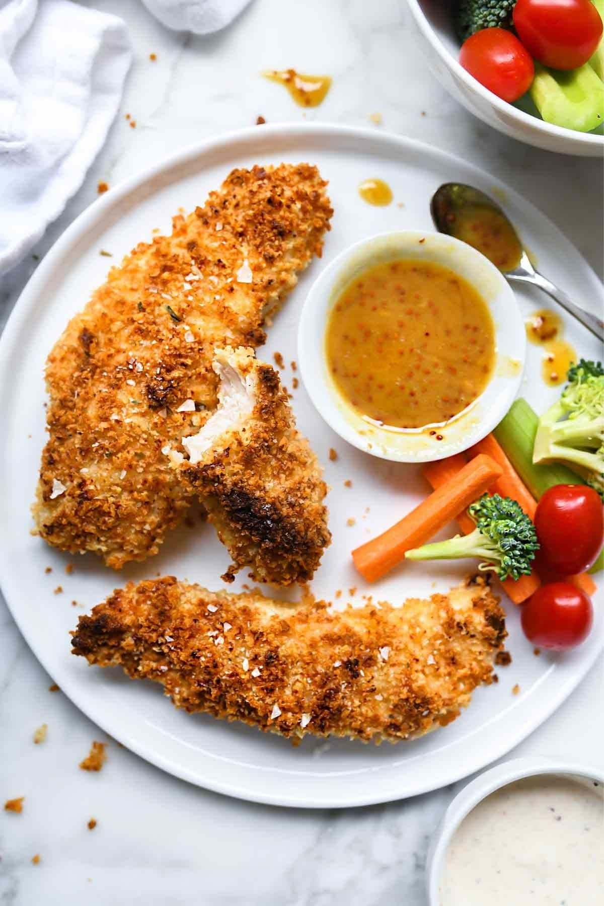 Chicken tenders on white plate with vegetables and honey mustard dip