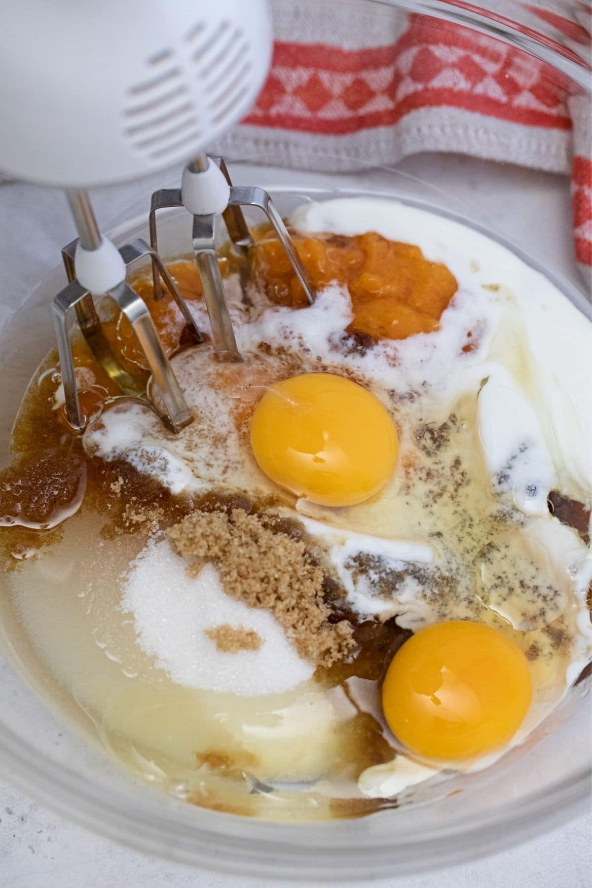 Glass bowl of batter with eggs on top and mixer in side