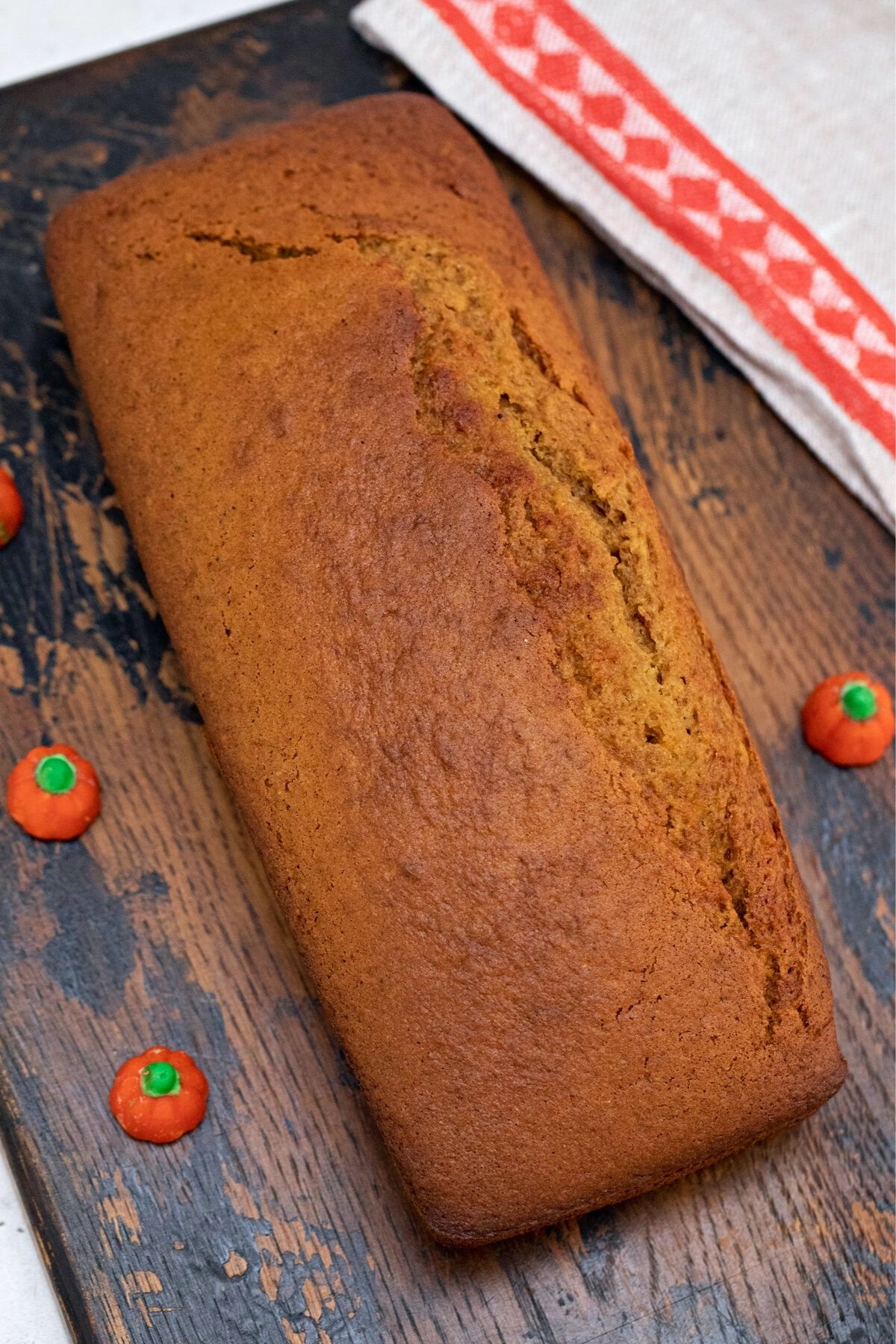 Whole loaf of pumpkin bread on dark wood cutting board by red and white napkin