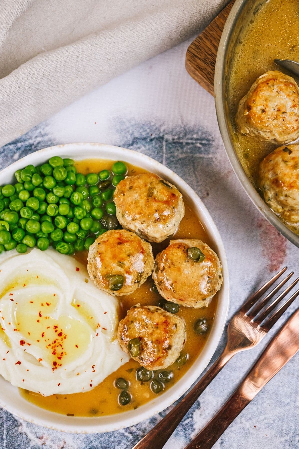 Bowl of meatballs with potatoes and peas next to skillet of chicken piccata meatballs