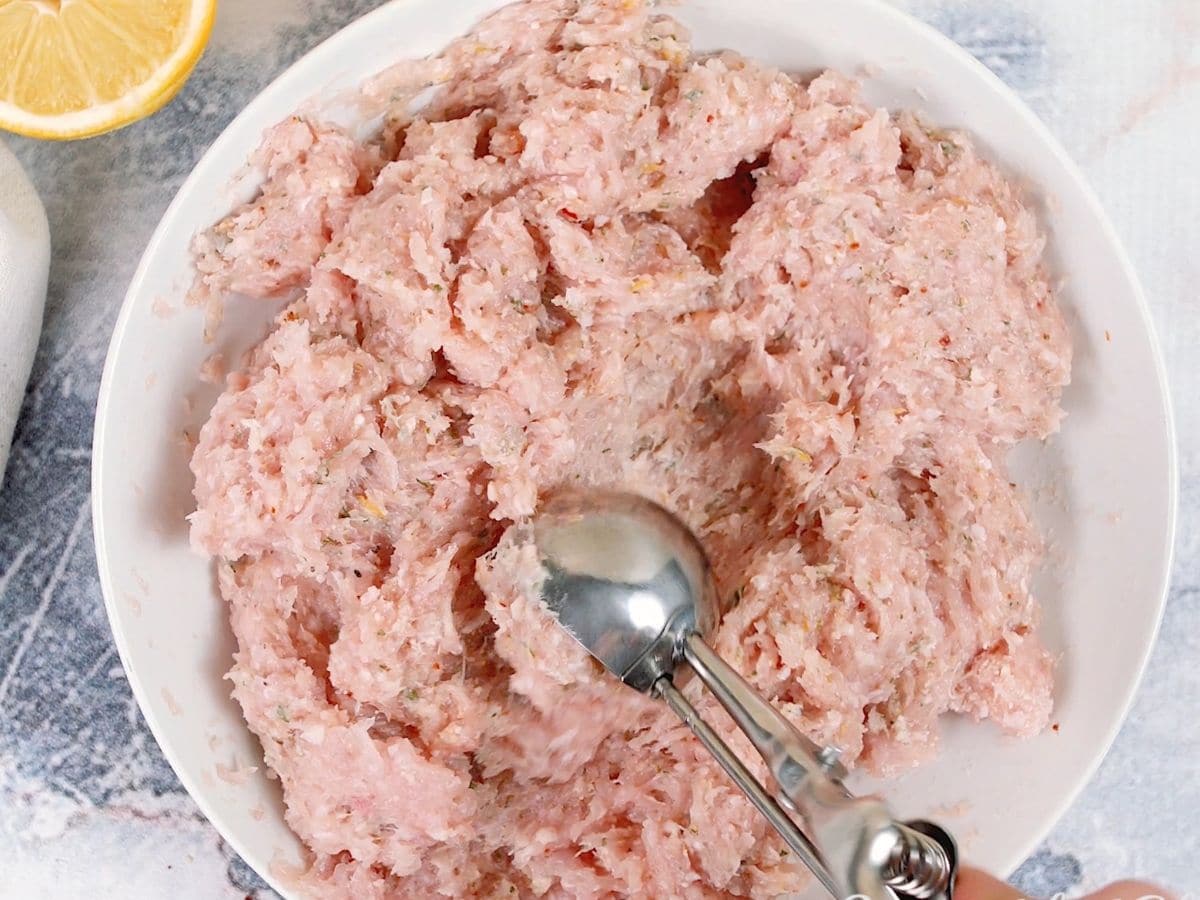Cookie scoop in bowl of raw ground meat mixture