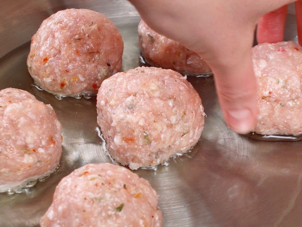 Hand placing meatballs into stainless steel skillet