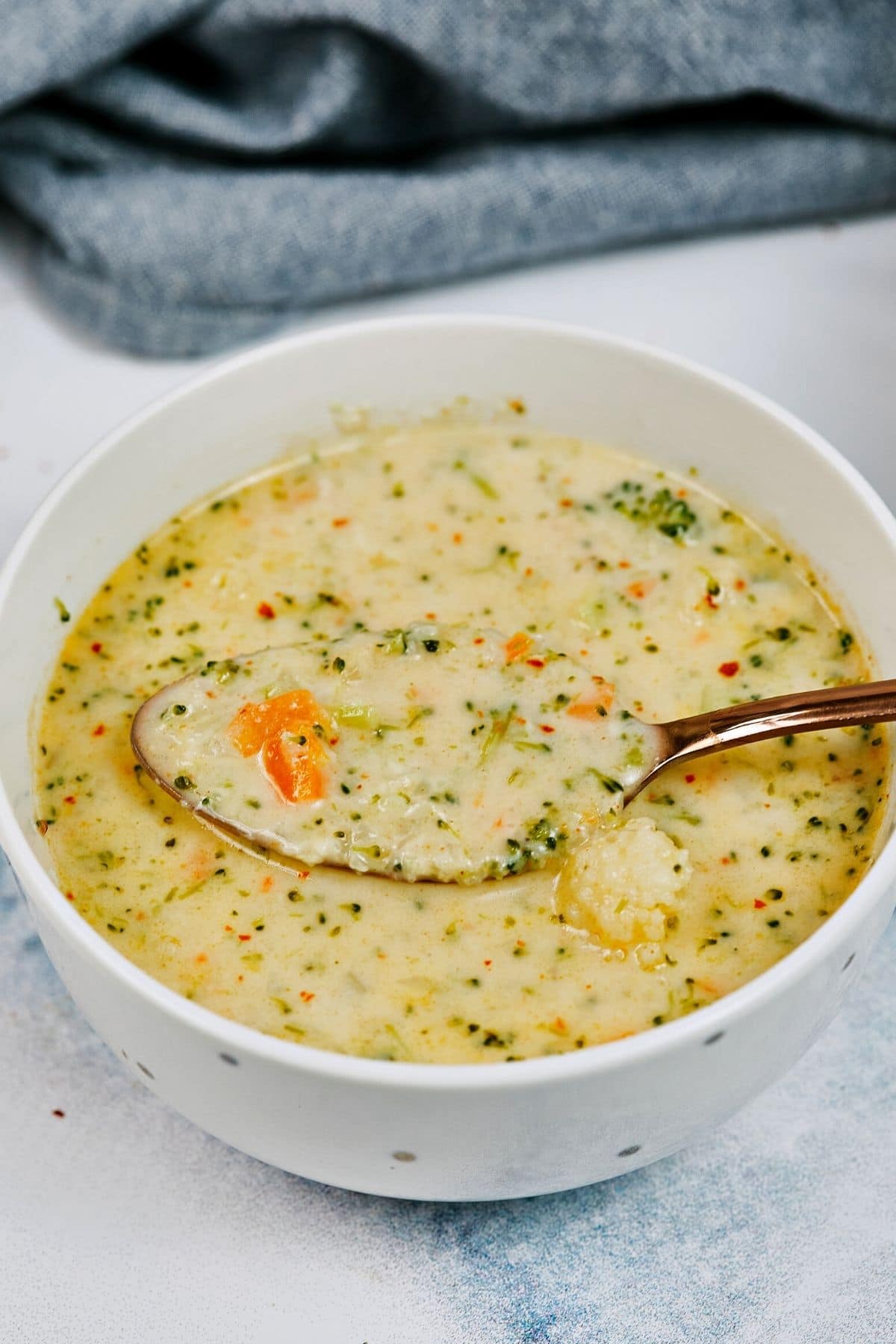 White bowl of cheese soup with spoon hovering over holding carrot