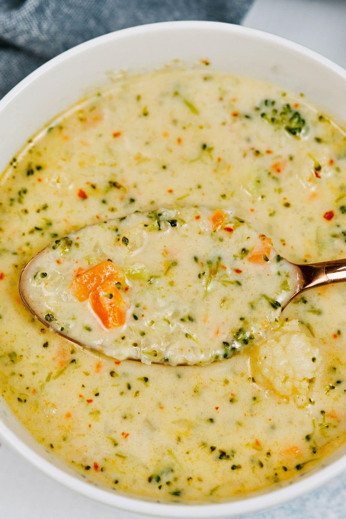 Close up image of spoon in bowl of cheese soup with broccoli and carrots