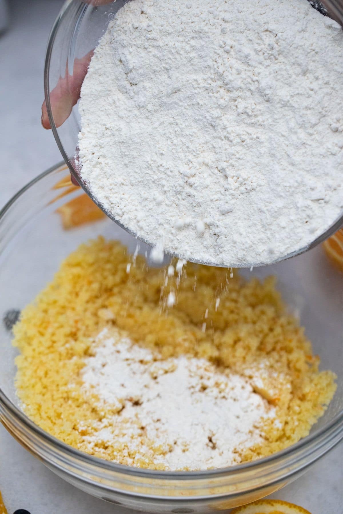 Hands pouring dry ingredients into bowl of egg and sugar