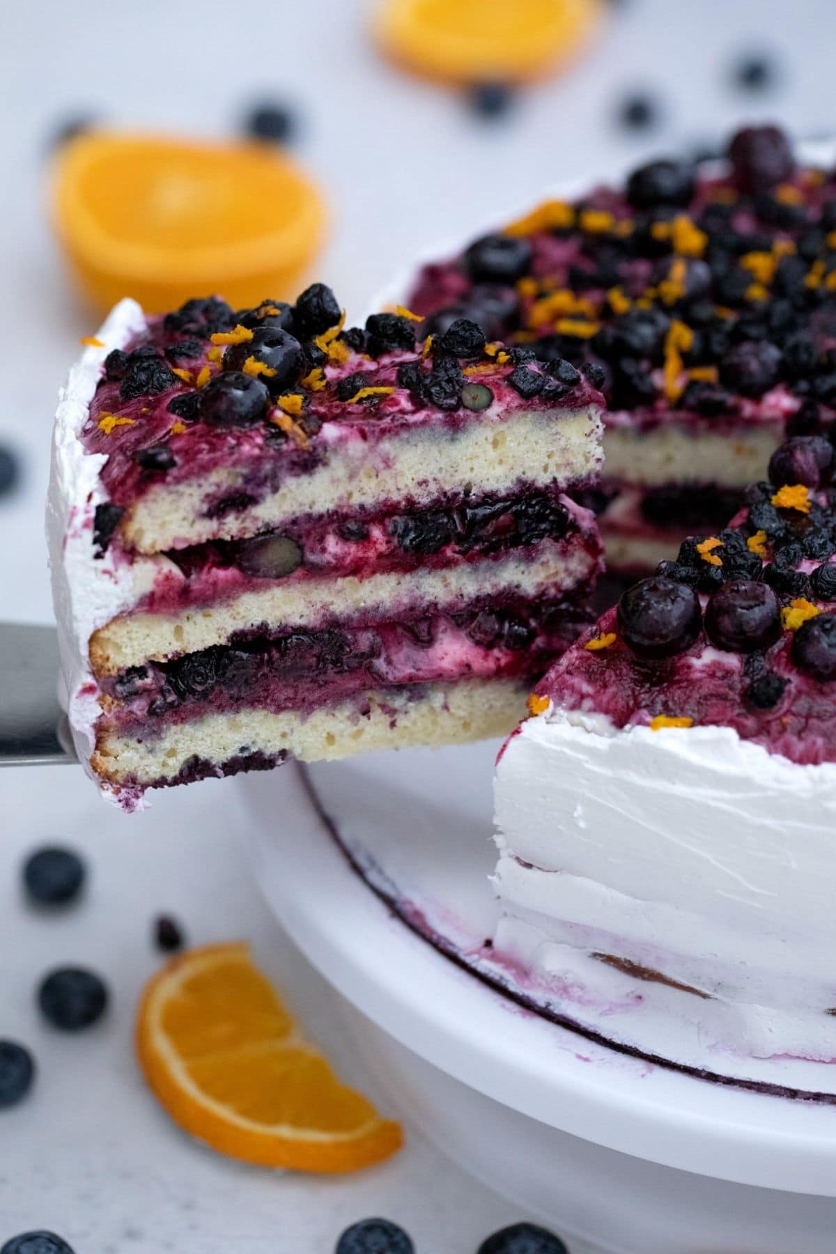 Slice of blueberry layer cake on cake spatula over cake stand