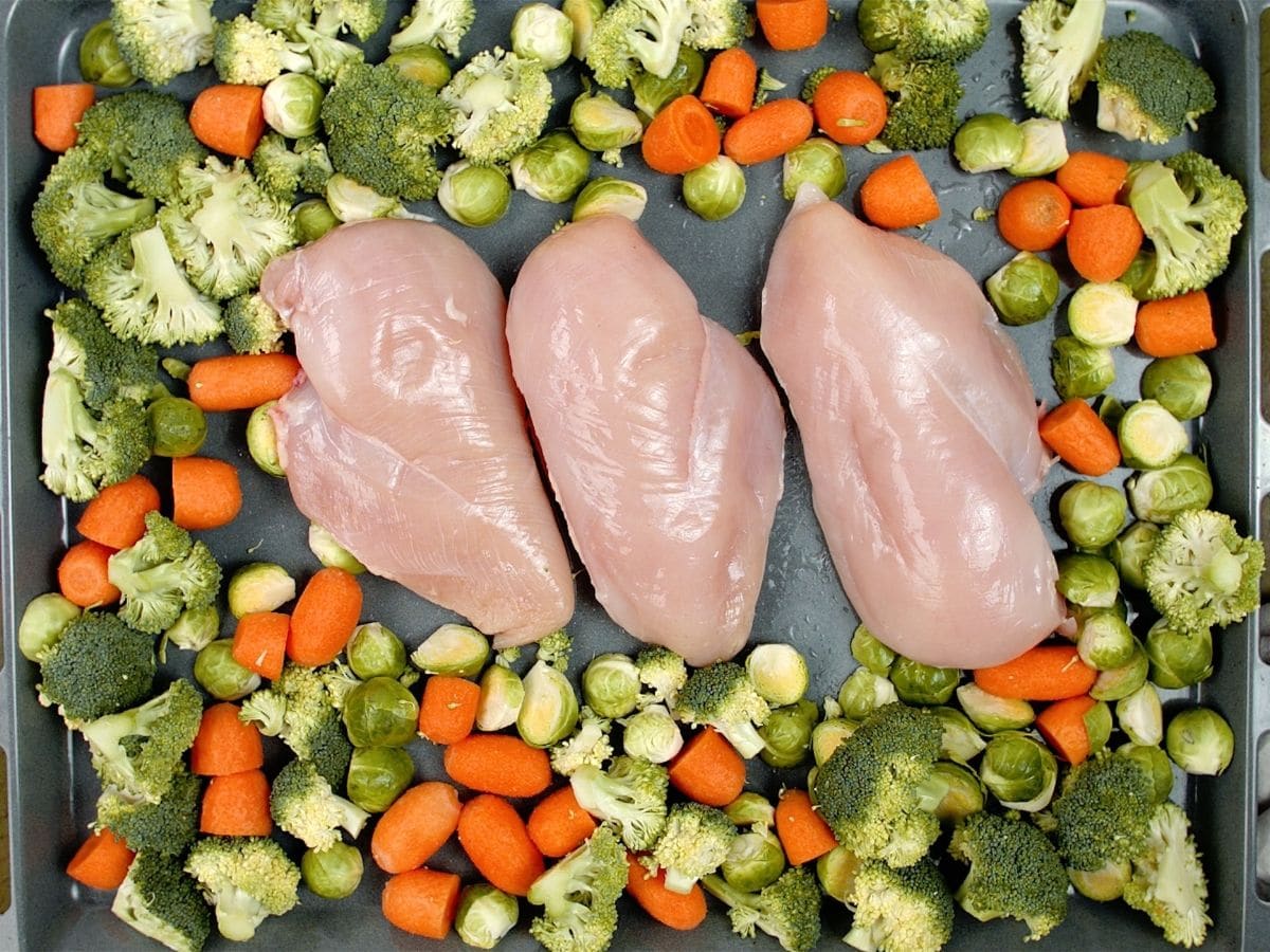 Raw chicken breasts in center of baking sheet with vegetables around the side