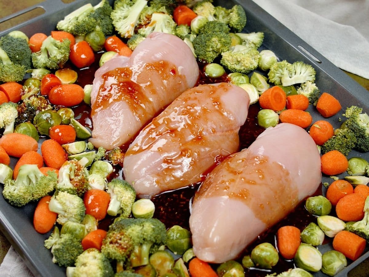 Sauce over raw chicken and vegetables on baking sheet