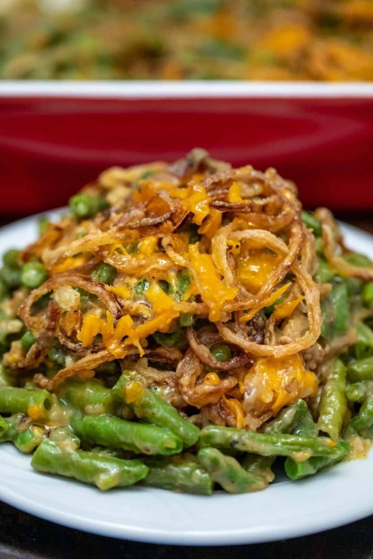 white plate of green bean casserole with red dish in background