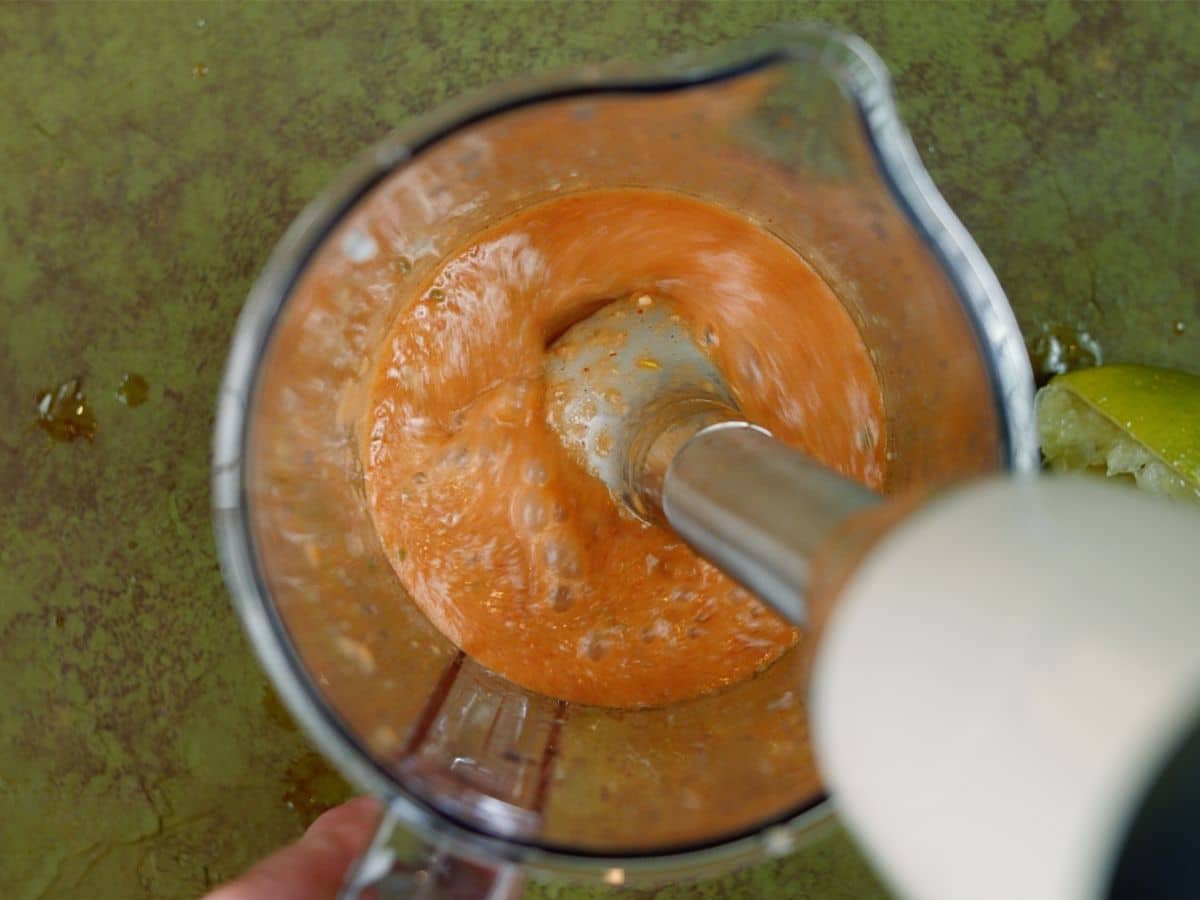 Immersion blender in measuring cup with orange liquid