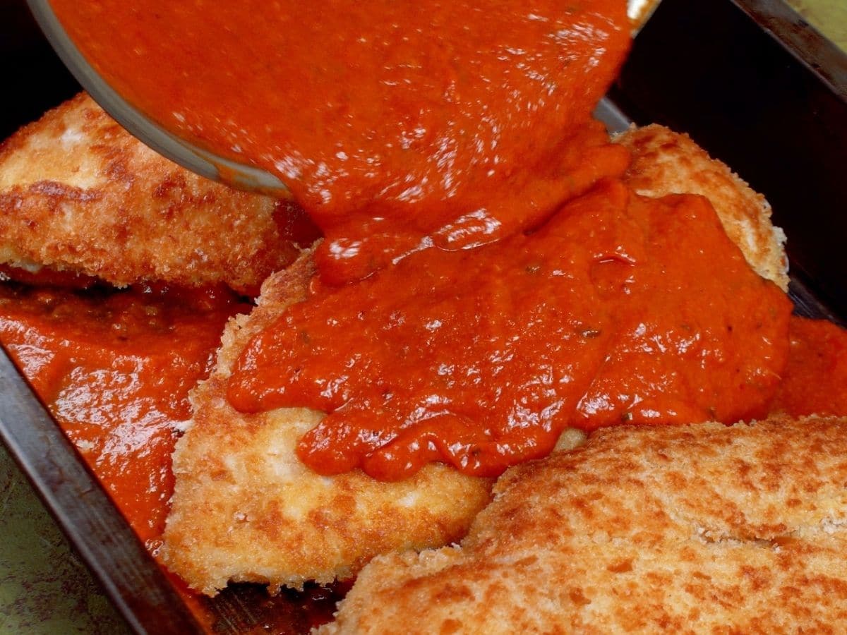 Tomato sauce being poured over fried chicken