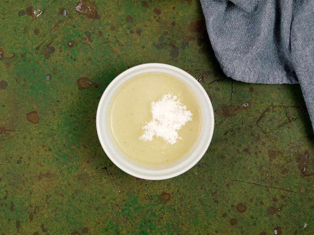 White bowl of corn starch and broth on green table