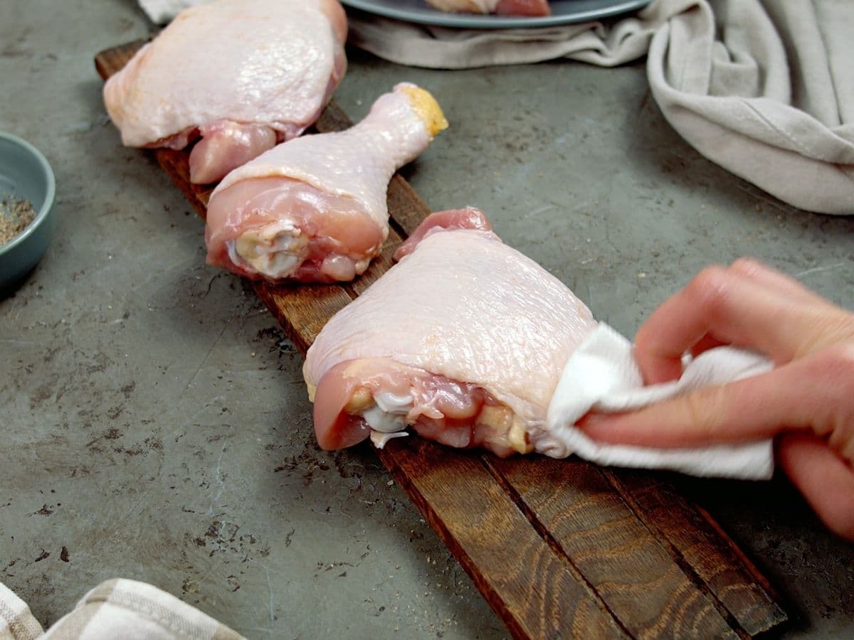 Hand using paper towel to dry chicken thigh