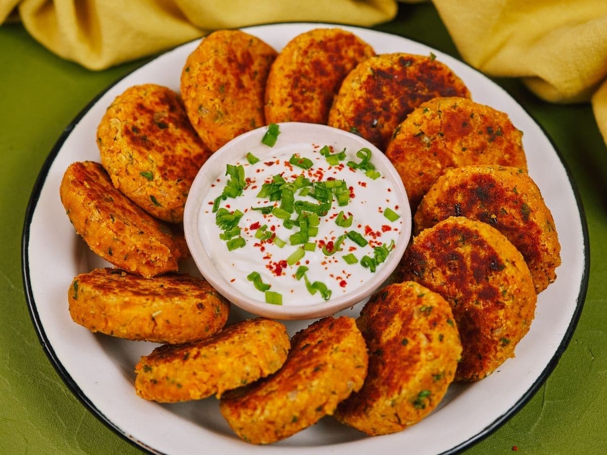 Round white plate of lentil patties with bowl of dip in the center