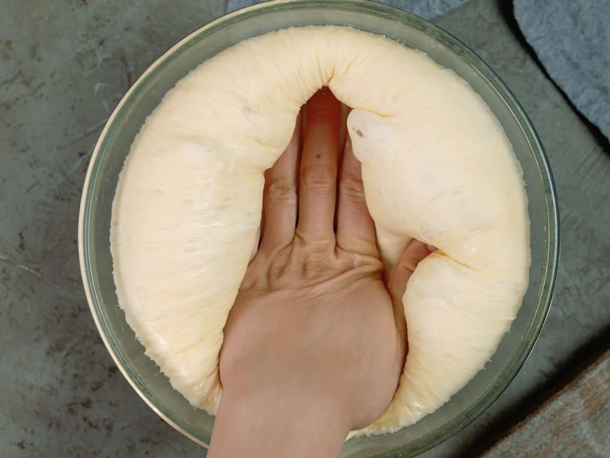 hand in the middle of risen bread dough in glass bowl