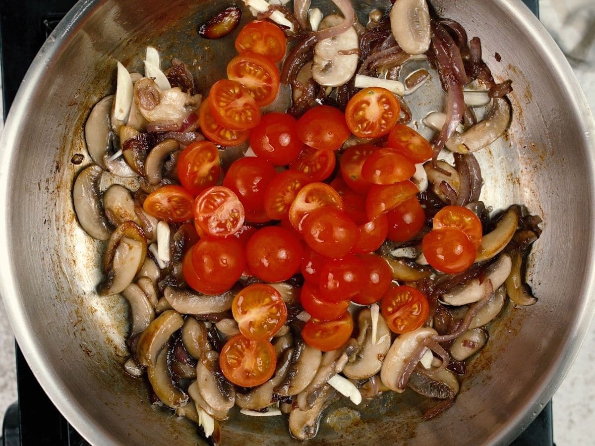 Tomatoes on top of cooked mushrooms in skillet