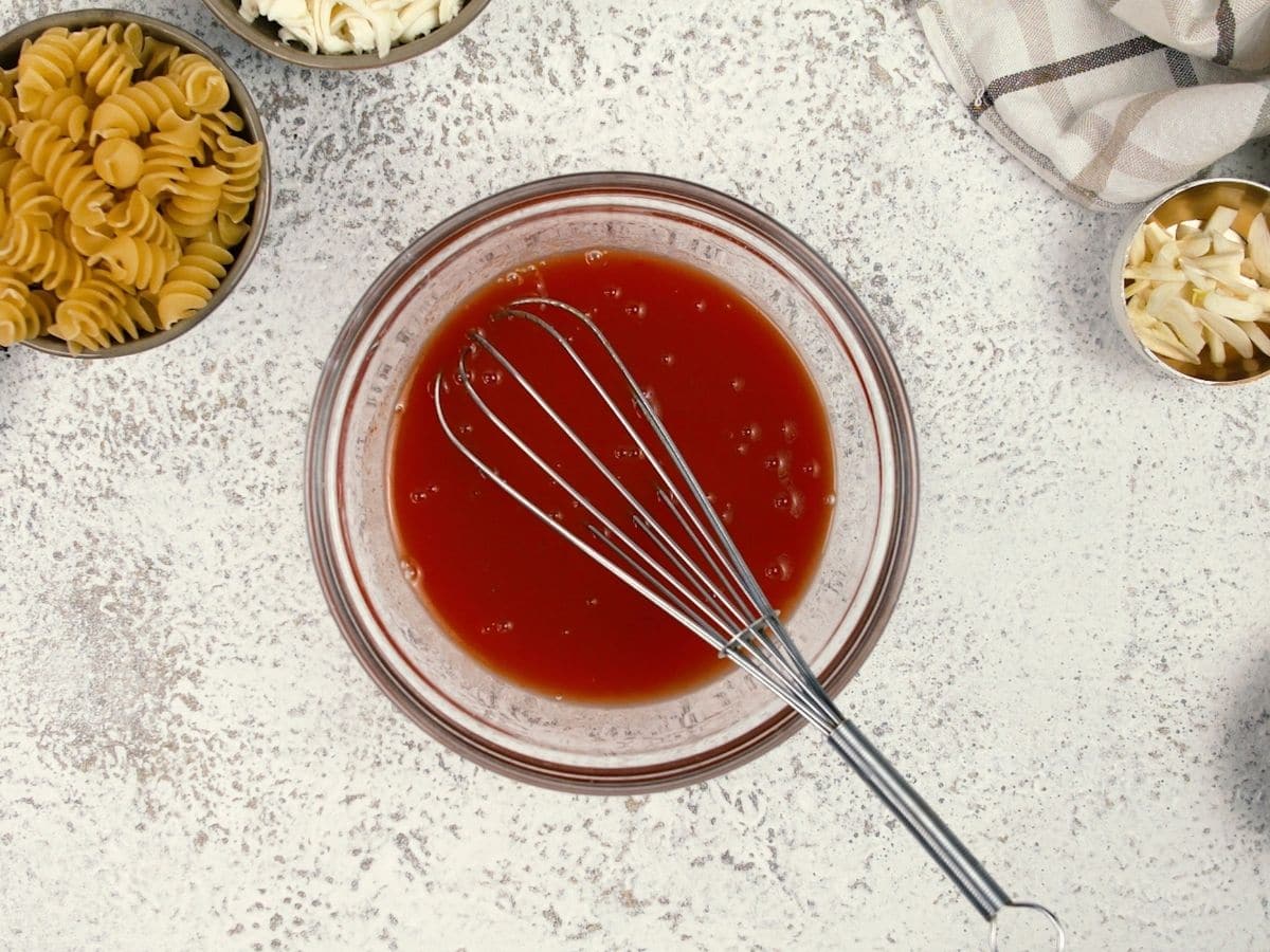 Whisk in cup with tomato sauce on marble table