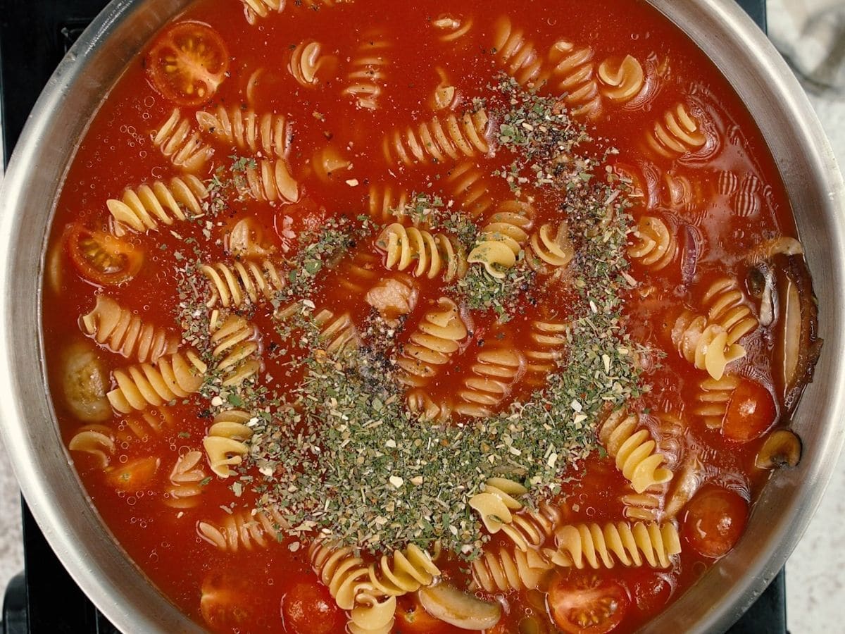 Tomato sauce over raw pasta with herbs in skillet