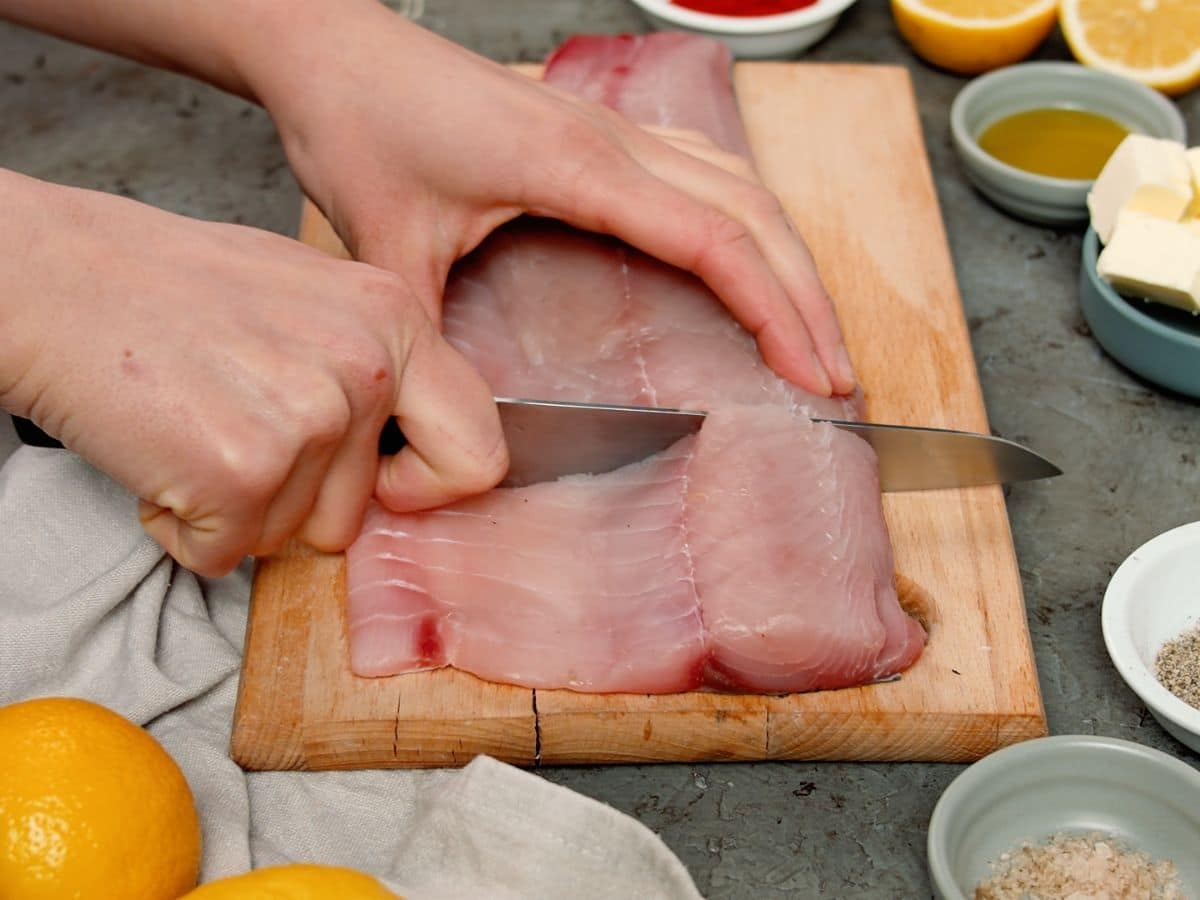 Hand using knife to cut through fish