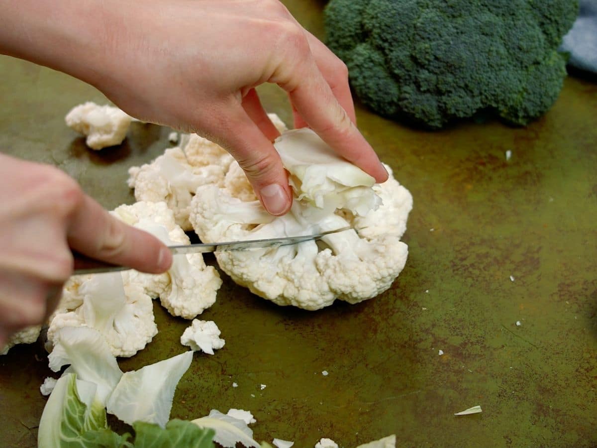 hand cutting head of cauliflower on green table next to broccoli