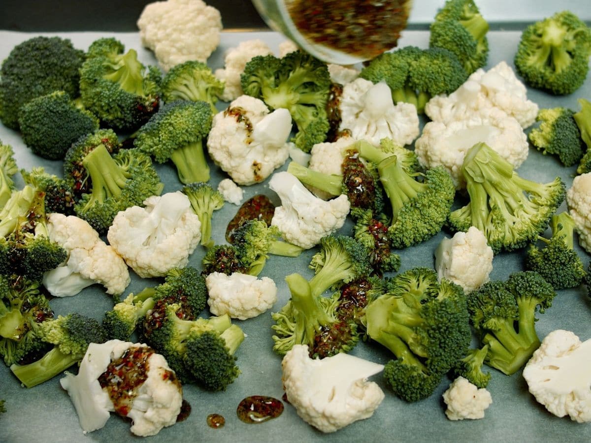 Bowl of sauce being poured over broccoli and cauliflower