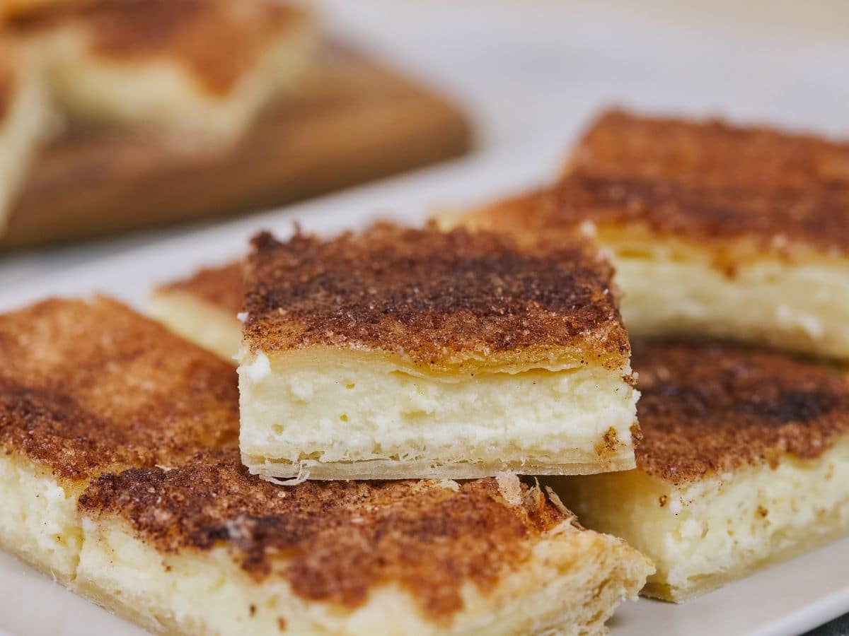Square cheesecake slices with cinnamon sugar tops stacked on white platter