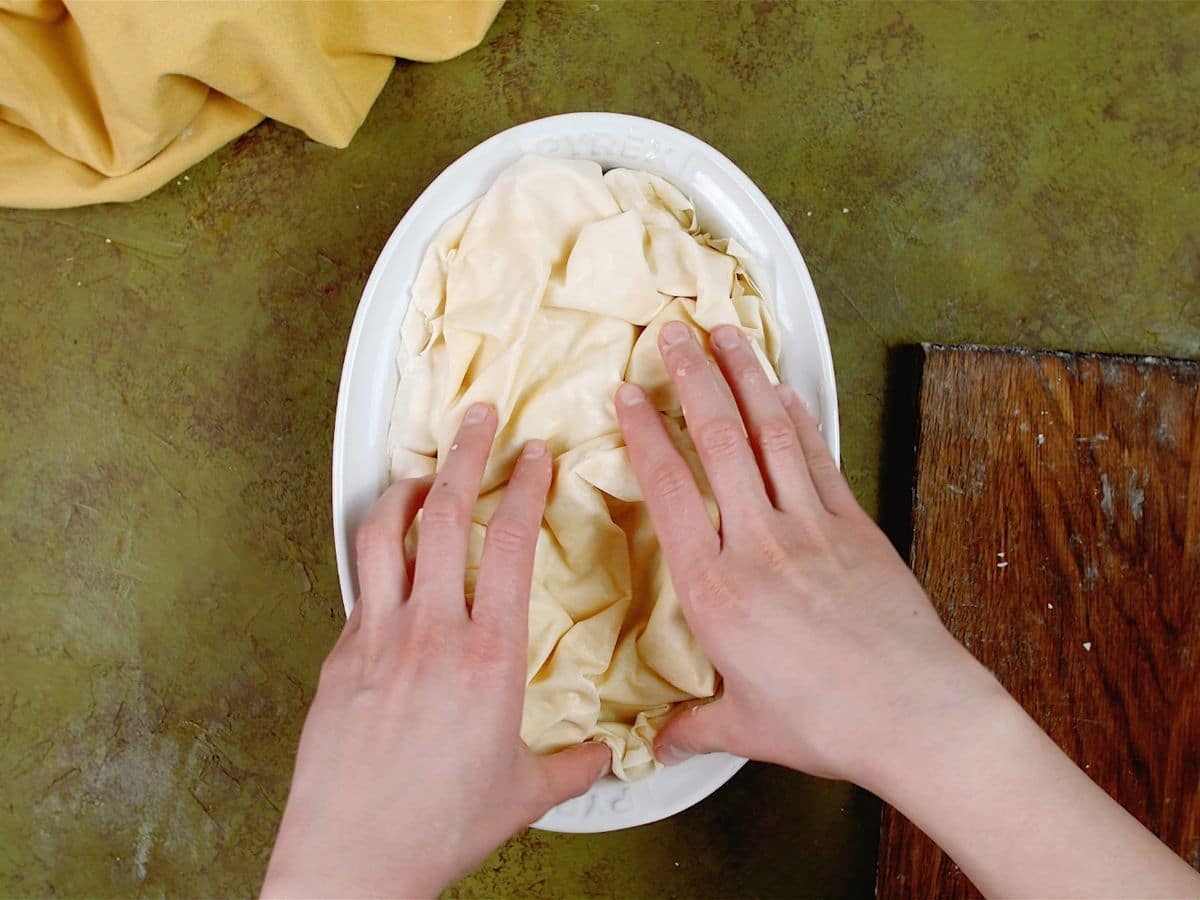 hands crumpling phyllo dough over top of meat and cheese filling