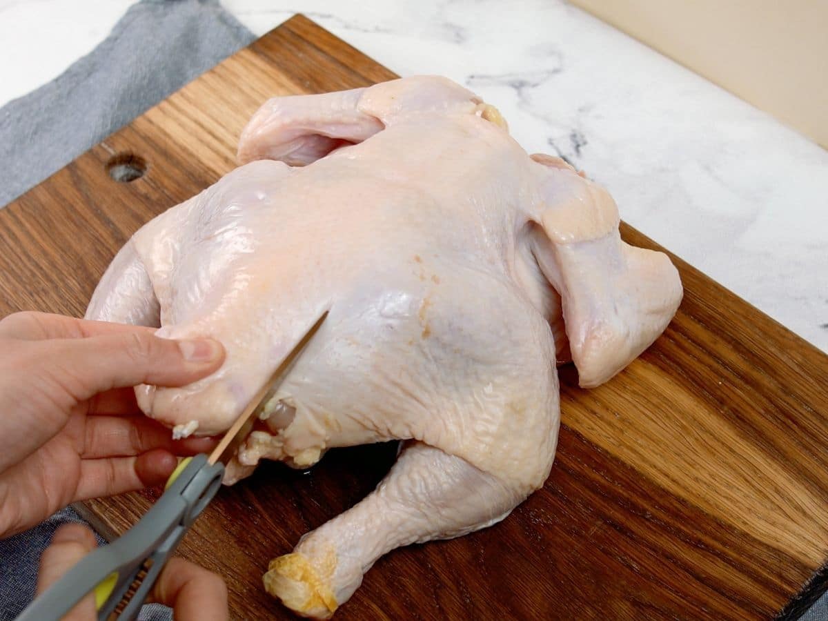 Scissors cutting through skin on raw whole chicken