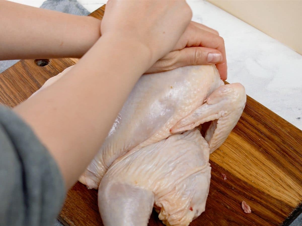 Hands clasped together on top of raw chicken on cutting board