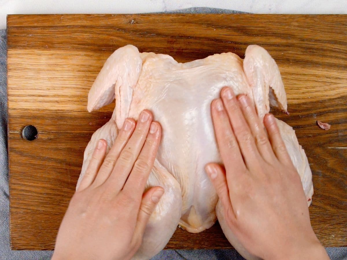 Hands pushing down on chicken breasts