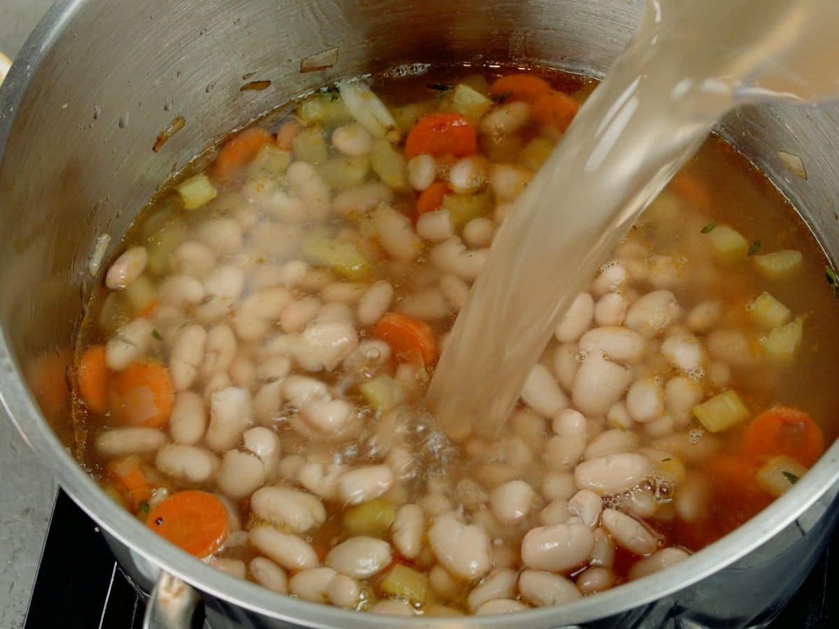 Broth being poured into pot with beans and carrots