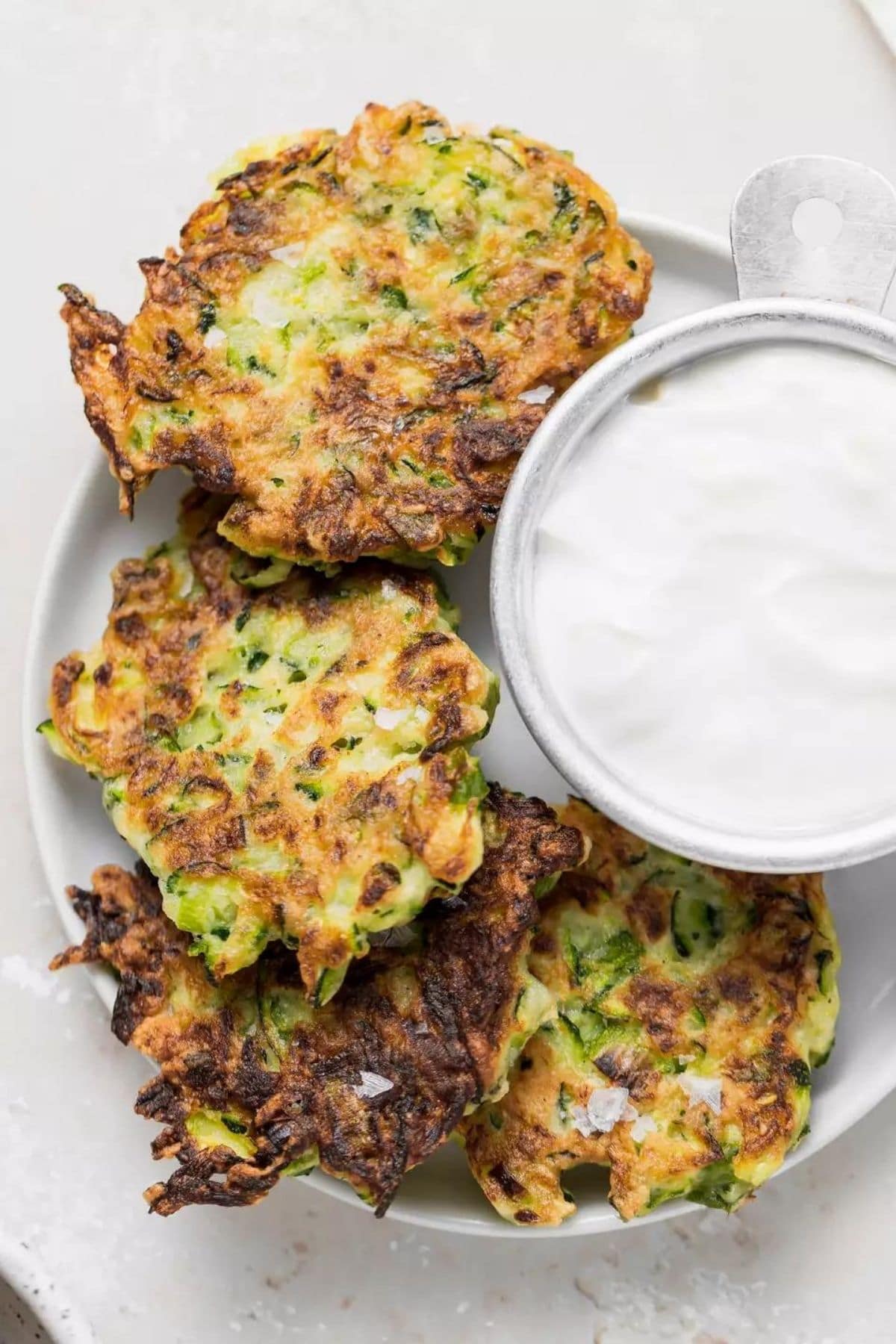 White platter of zucchini fritters with bowl of sauce