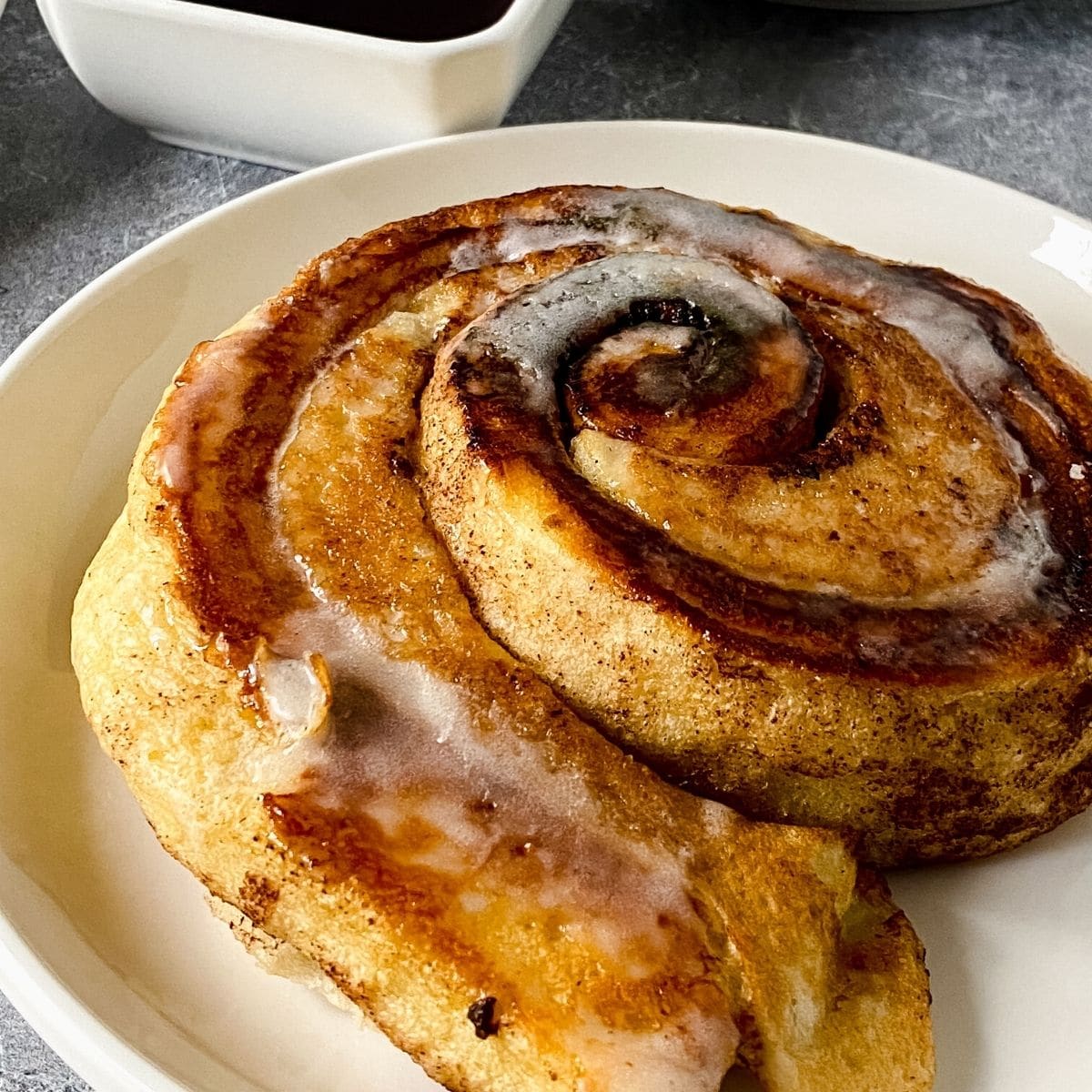 cinnamon roll pancake on white plate by bowl of syrup