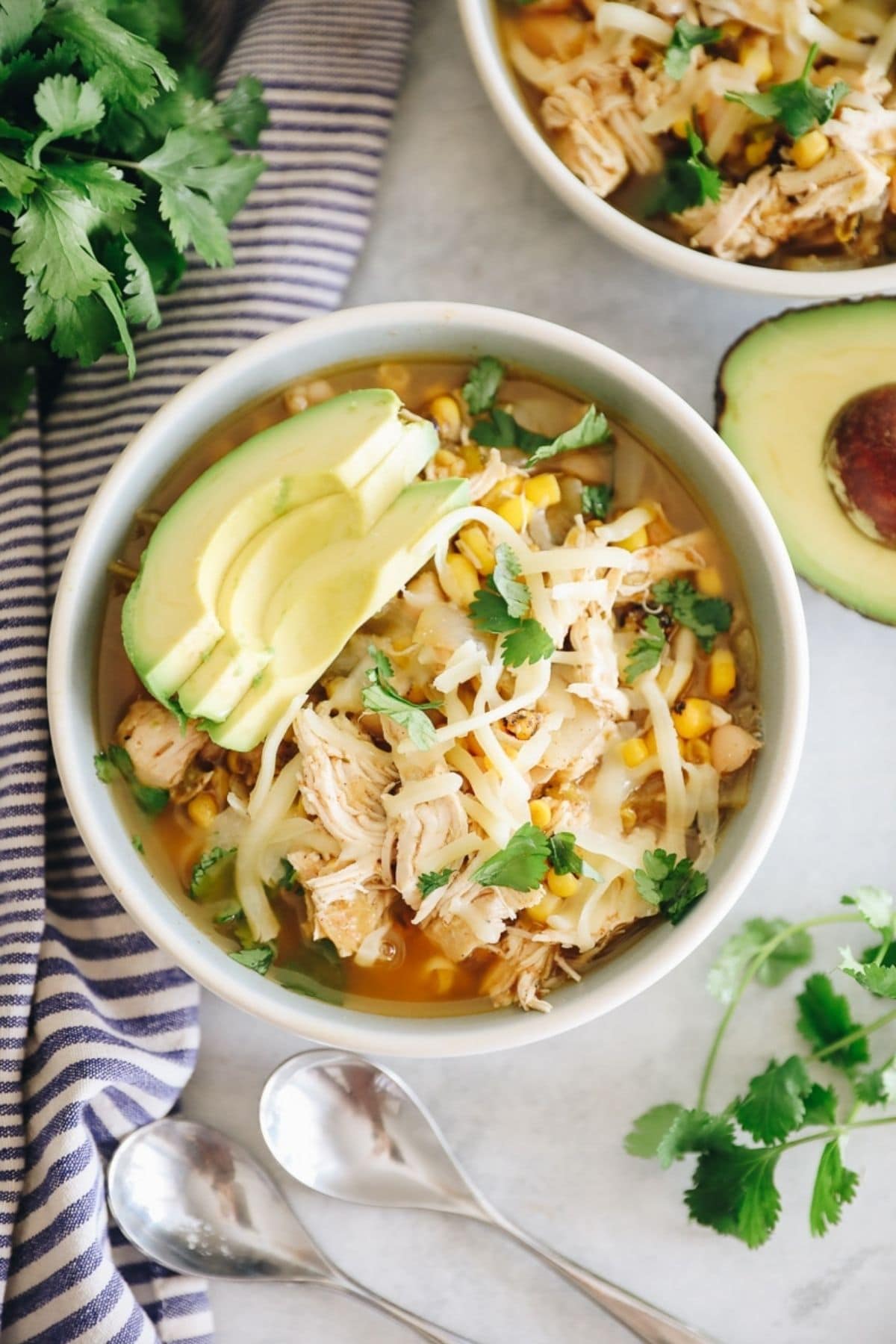 white bowl of chicken chili with sliced avocado on top