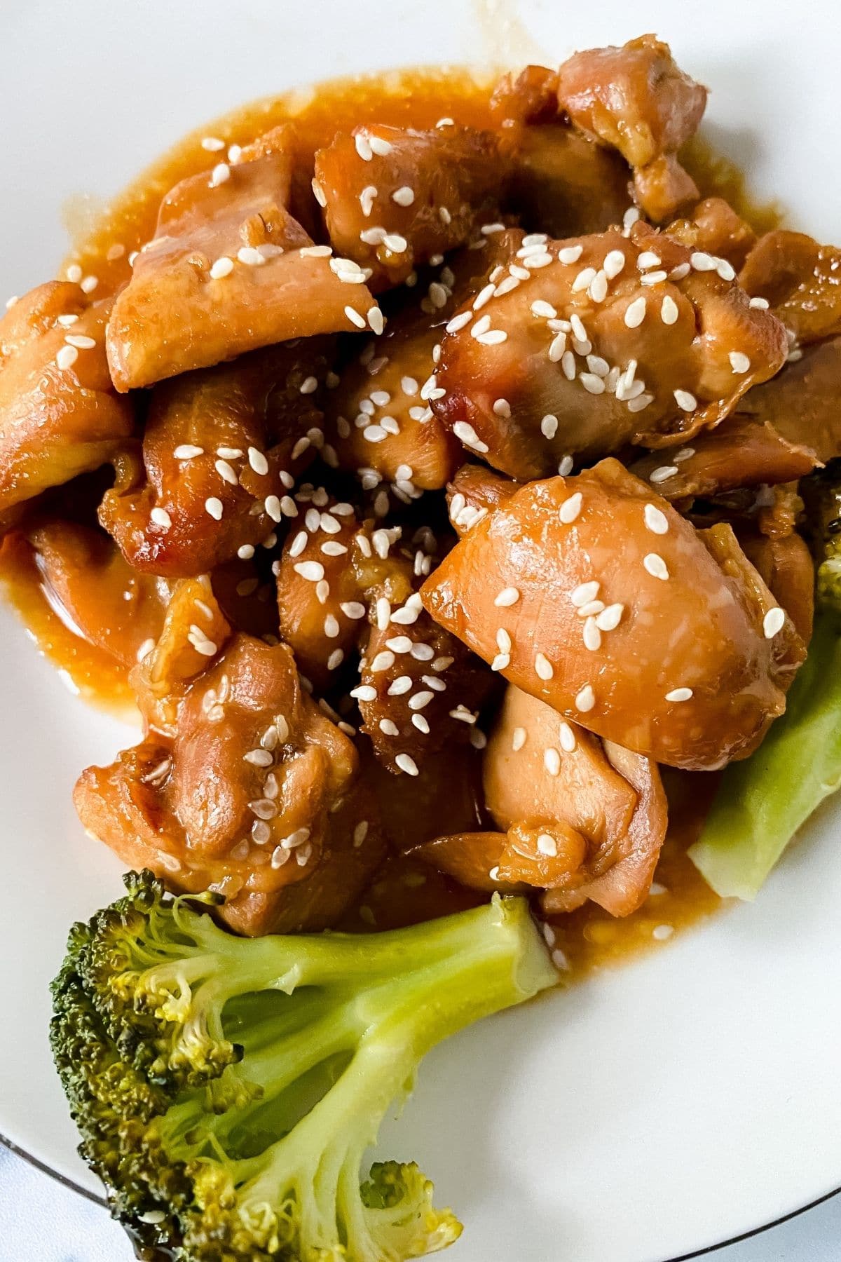 chicken in sauce on white plate with broccoli and sesame seed garnish
