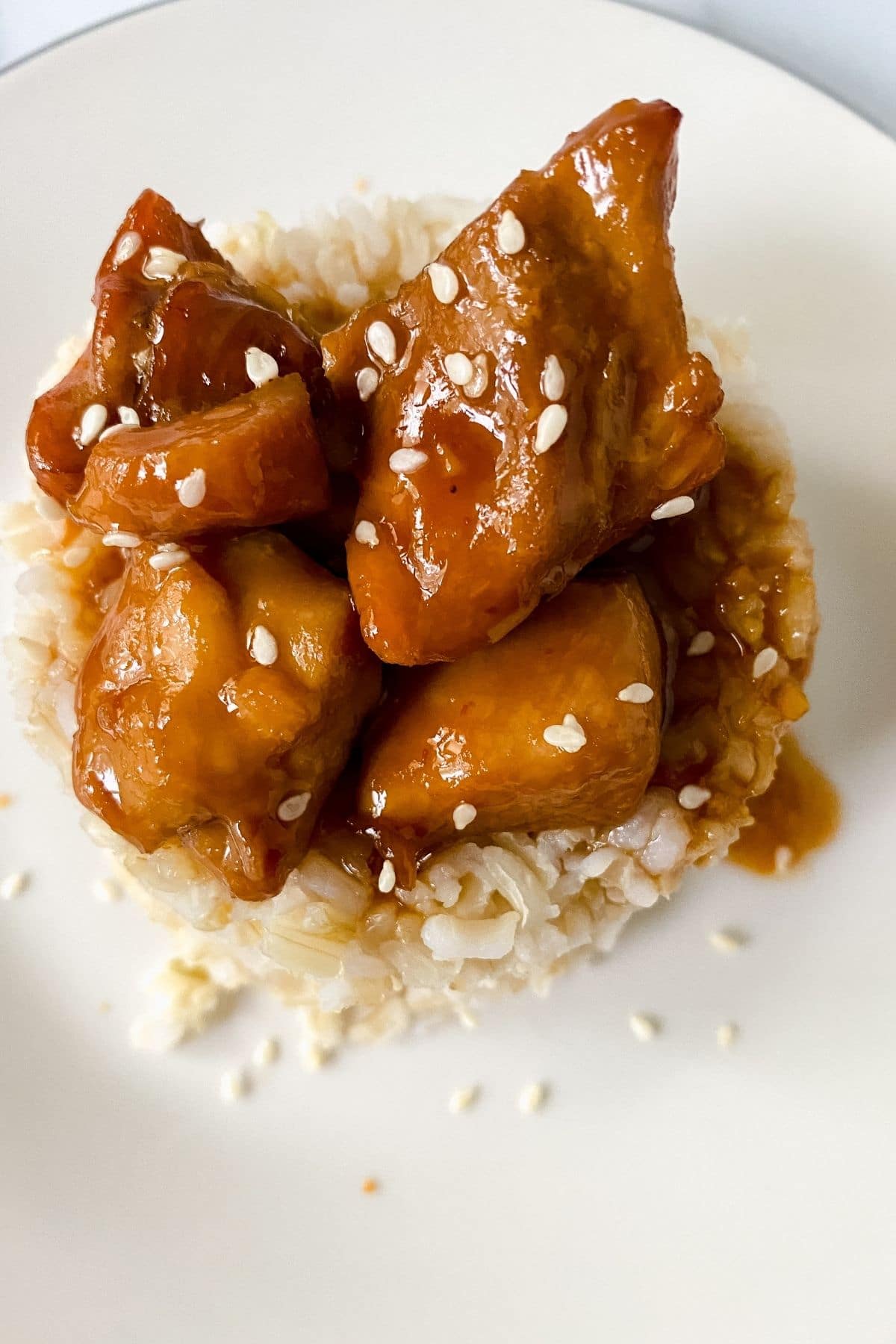 sesame chicken on pile of rice on white plate