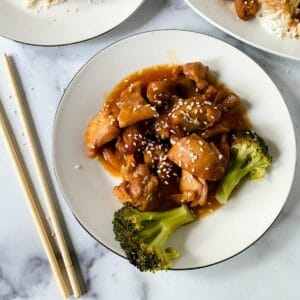 white plates of chicken in sauce on marble counter with chopsticks on side