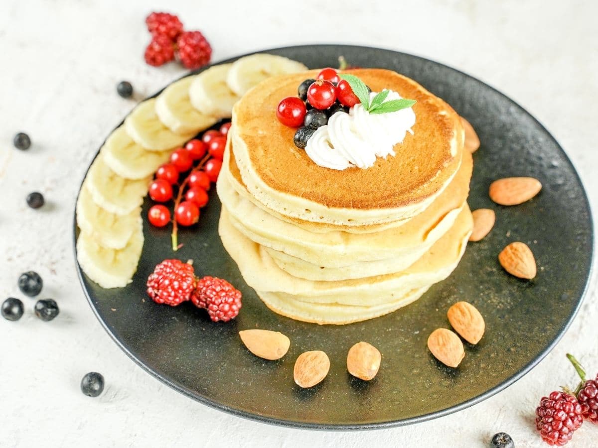 stack of banana pancakes on black plate with sliced bananas almonds and berries