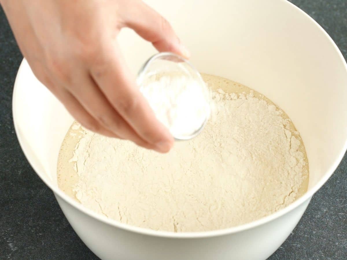 hand holding bowl of flour over bowl of pancake batter