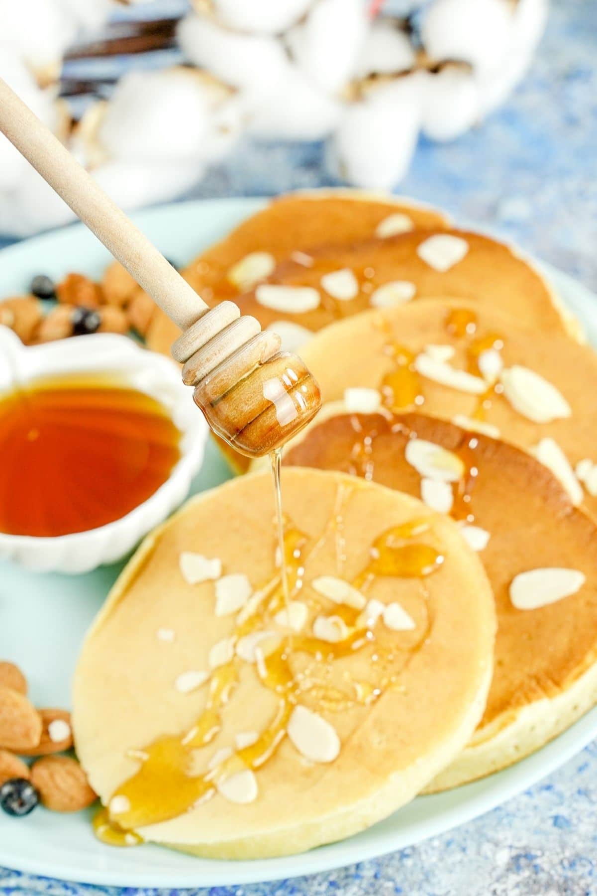 honey wand drizzling honey over the top of pancakes on blue plate