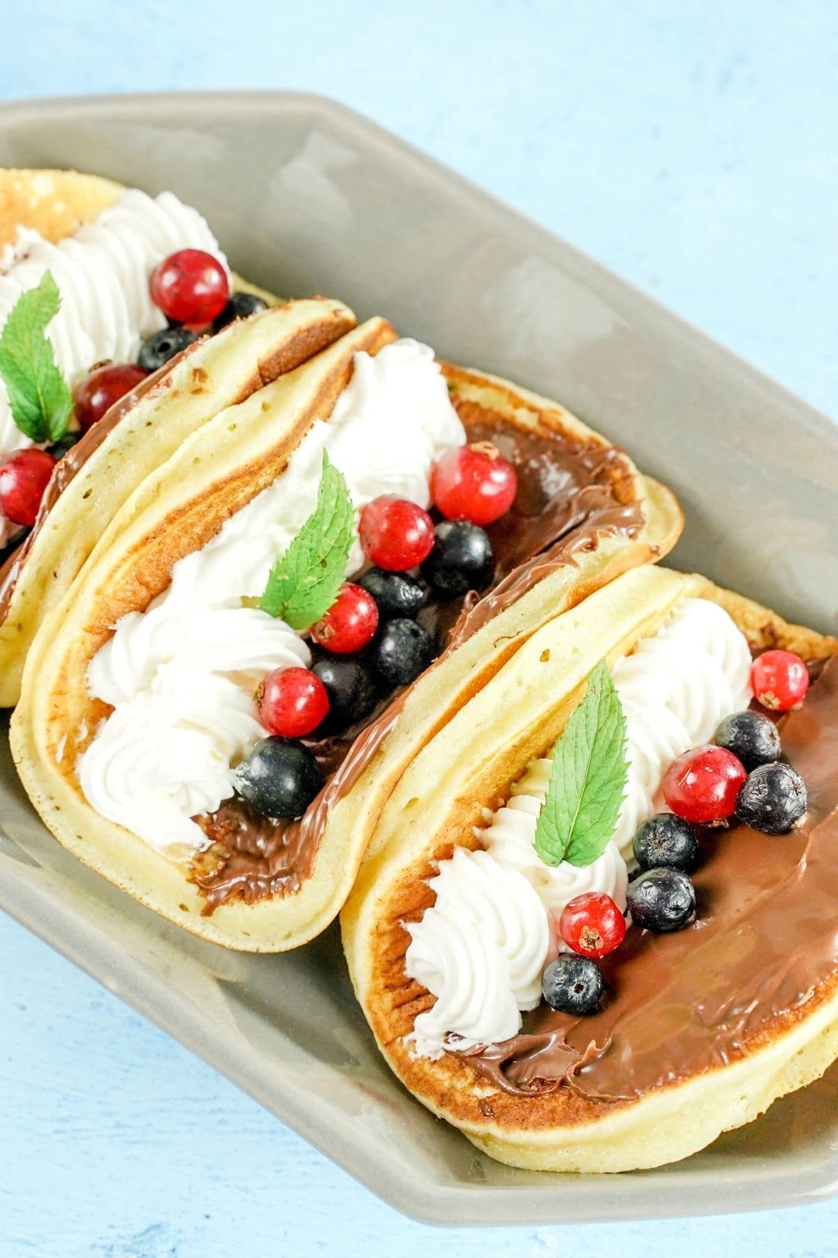 banana tacos stuffed with nutella berries and cream in gray platter on blue table