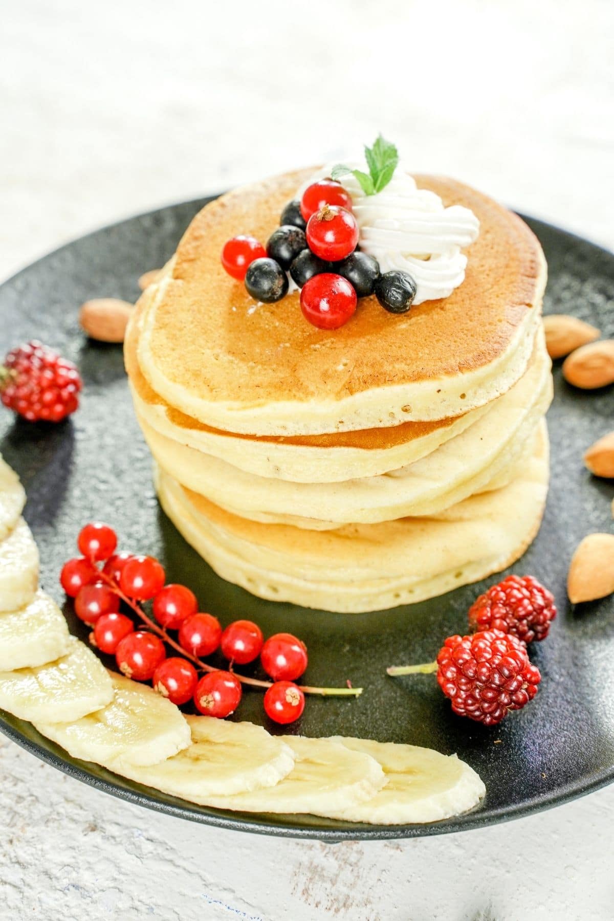 pancakes stacked on plate with berries and banana slices
