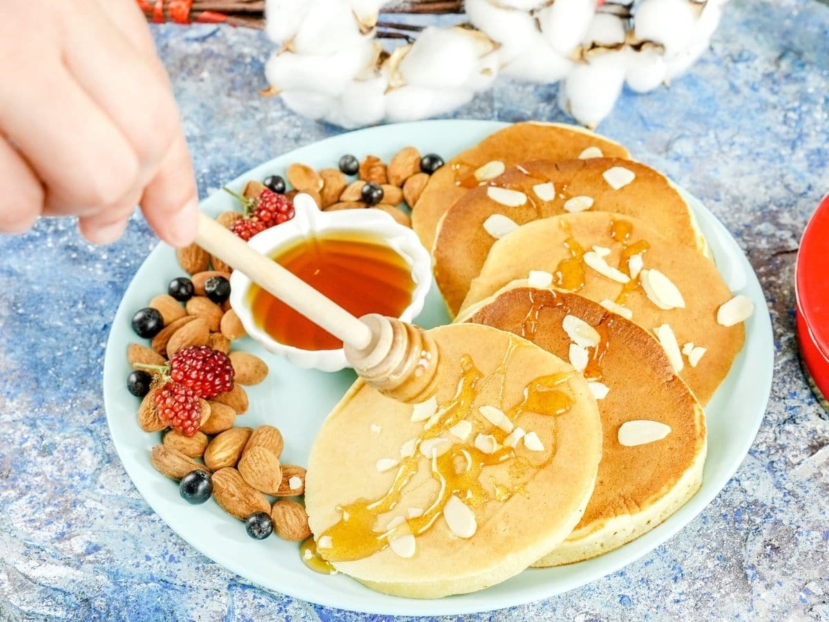 hand pouring honey over top of blue plate of pancakes