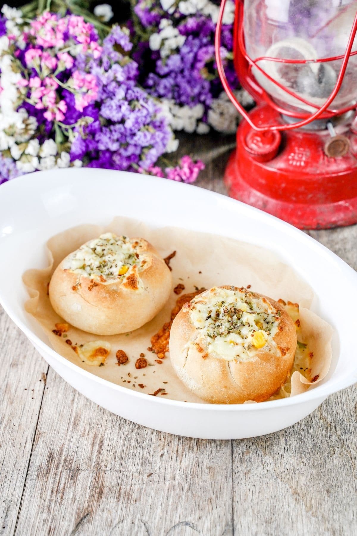oval white baking dish with two pizza buns inside on table with red lantern and purple flowers