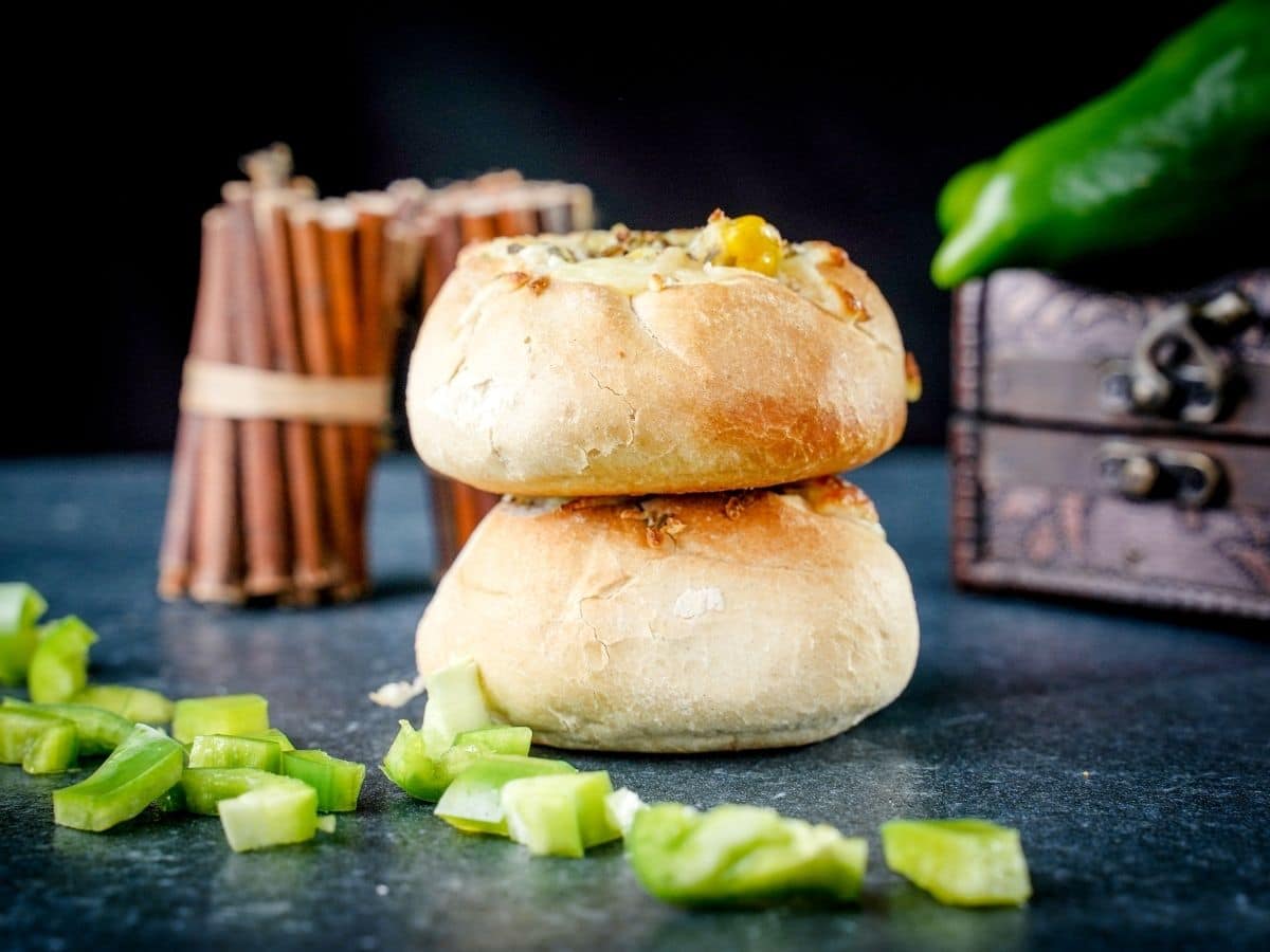 two pizza buns stacked on top of each other on black table by bundle of cinnamon sticks and bell peppers