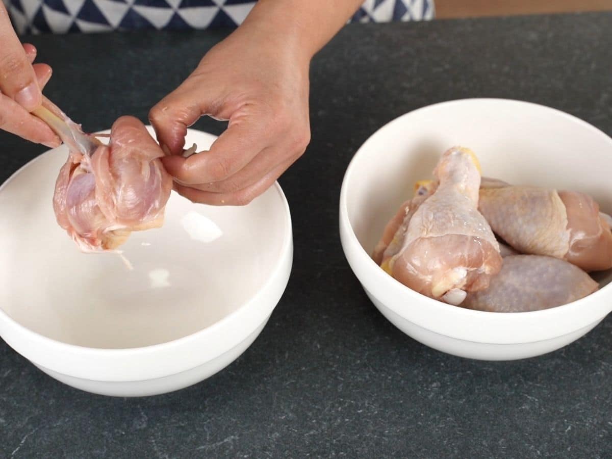 hands holding chicken leg over white bowl