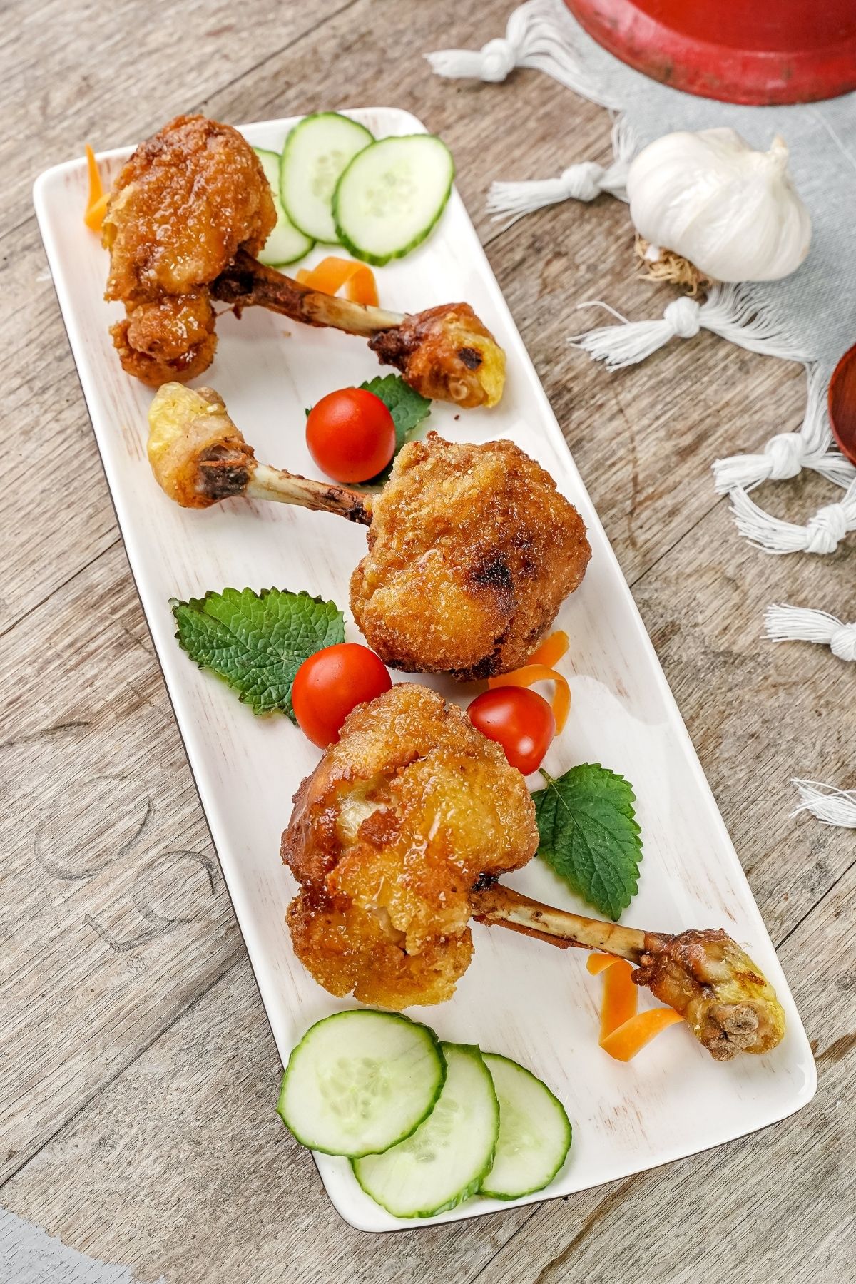 long white platter with three chicken lollipops and fresh basil and tomatoes laying on a wood table