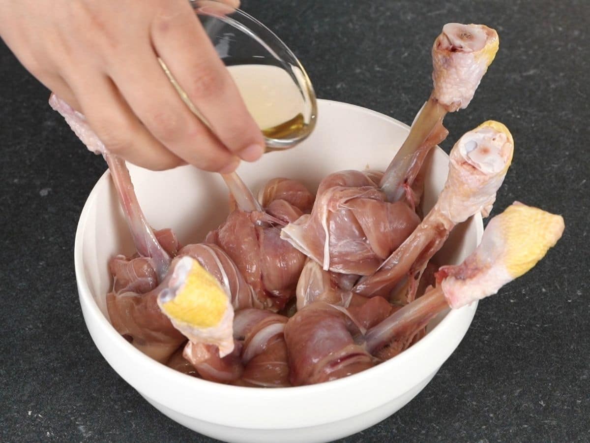 hand pouring white wine over chicken legs in white bowl